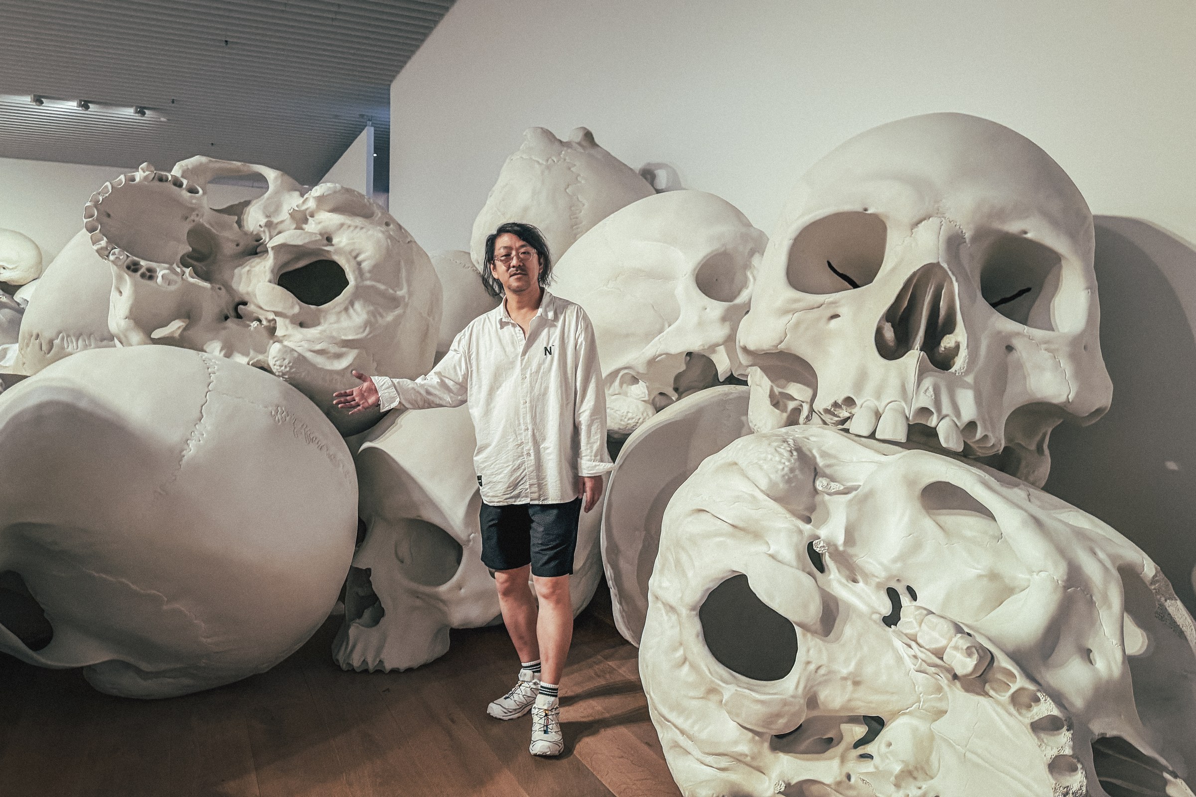 Tadahiro Koto standing among the skull sculptures of Ron Mueck’s Mass at Mori Art Museum, Tokyo